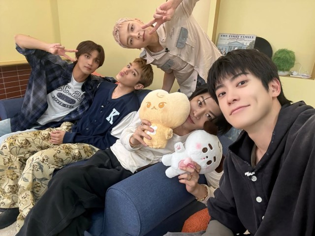 NCT 127 poses holding dolls in a cozy indoor setting revealing a comfortable daily life